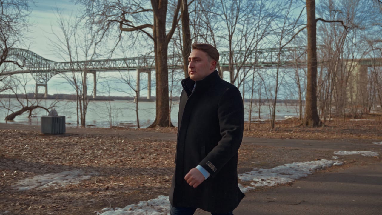 Lucas Beaulieu marche au bord du fleuve, un pont à l'arrière-plan
